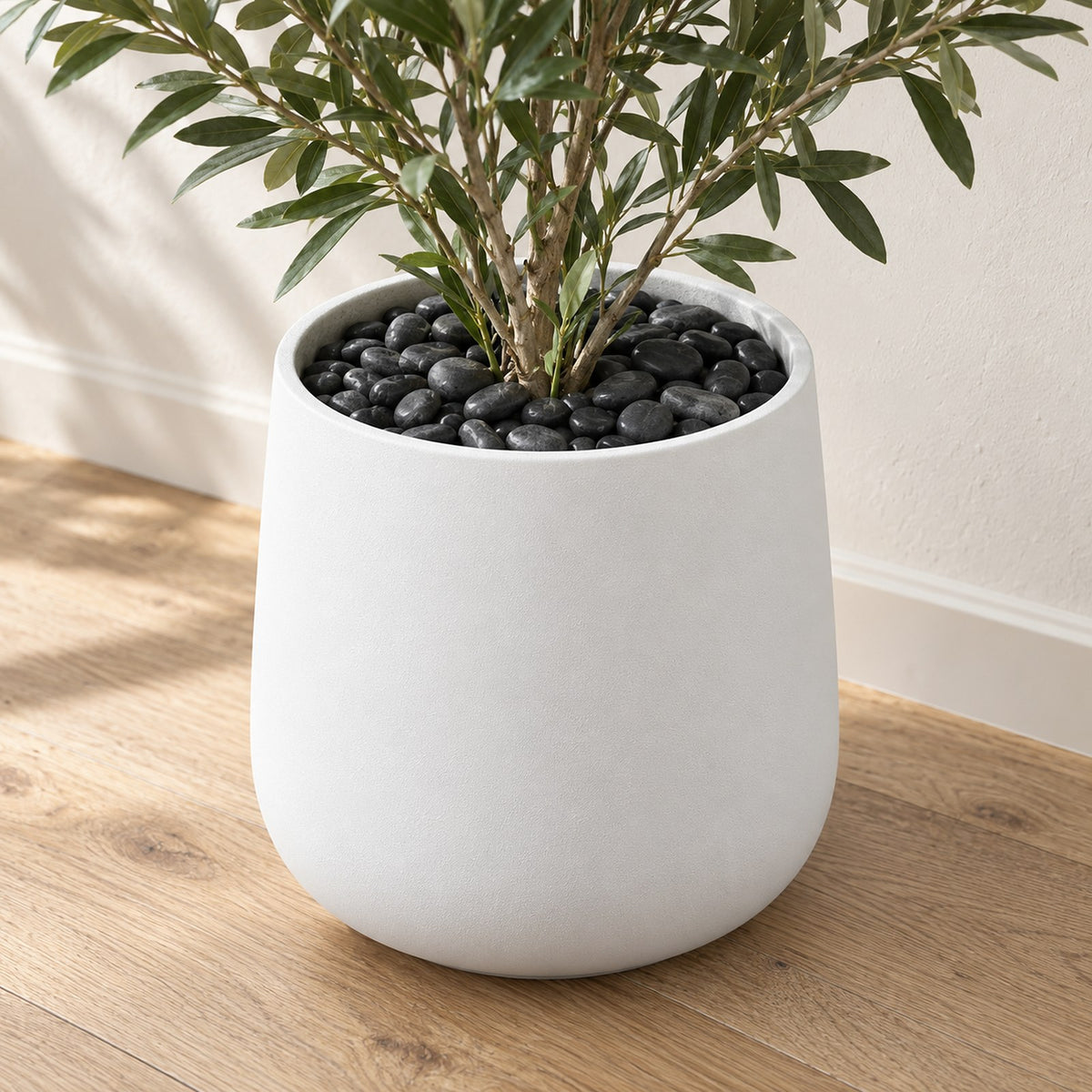Black River Pebbles covering the top of a white planter with a plant