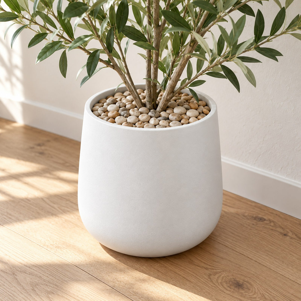 Natural River Pebbles covering the top of a white planter with a plant